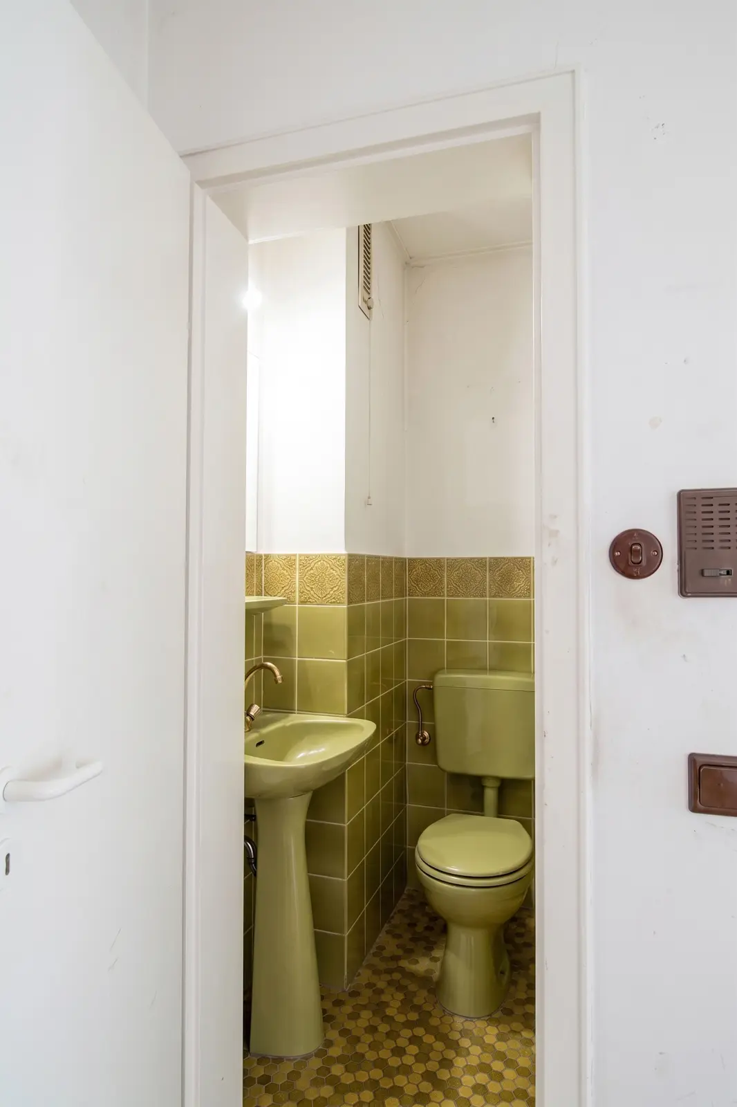 Ein kleines Badezimmer mit umweltfreundlichen Sanitäranlagen, darunter eine Toilette und ein Waschbecken, sowie grün gefliesten Wänden und Böden.
