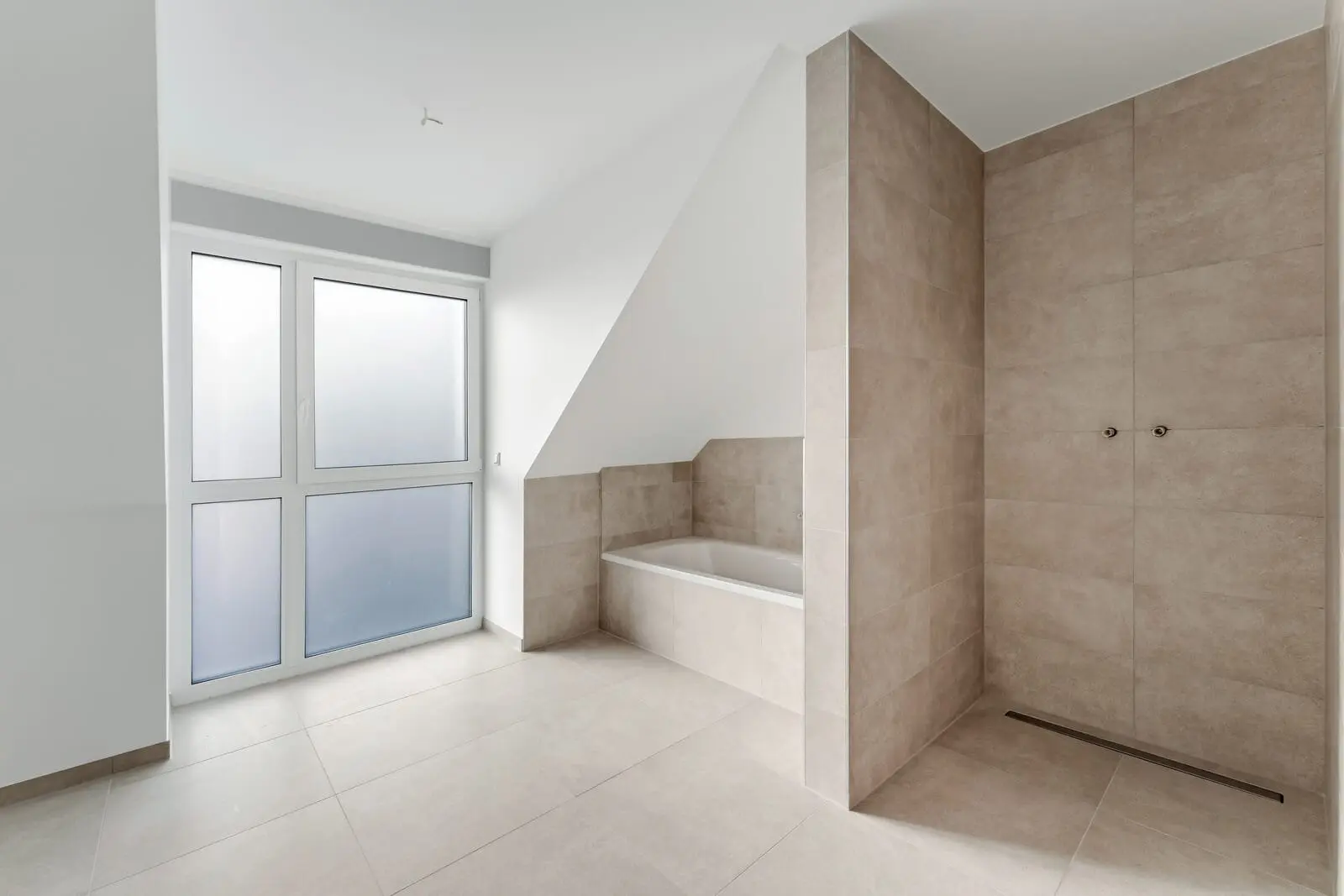 Modernes, minimalistisches Badezimmer mit beigen Fliesen, einer eingebauten Badewanne, einer begehbaren Dusche und großen Milchglasfenstern, die Tageslicht hereinlassen.