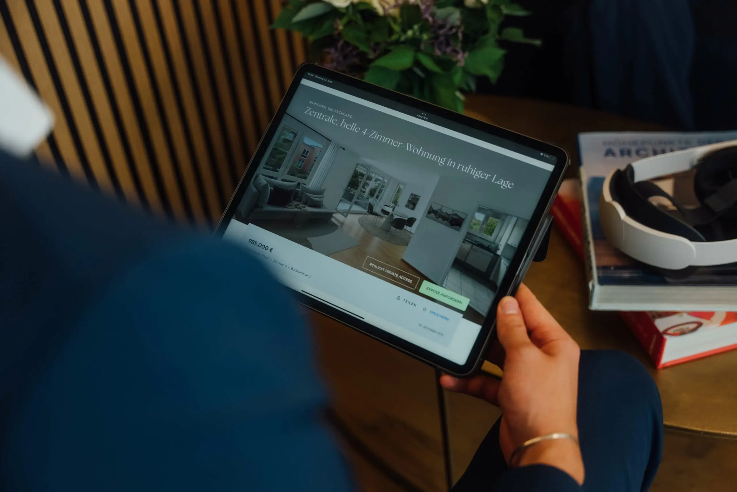 Eine Person hält ein Tablet in der Hand, auf dem stolz ein Immobilienangebot mit Bildern einer modernen Wohnung präsentiert wird. Erfahren Sie mehr über uns und erkunden Sie weitere atemberaubende Immobilien mit Ihren Fingerspitzen.