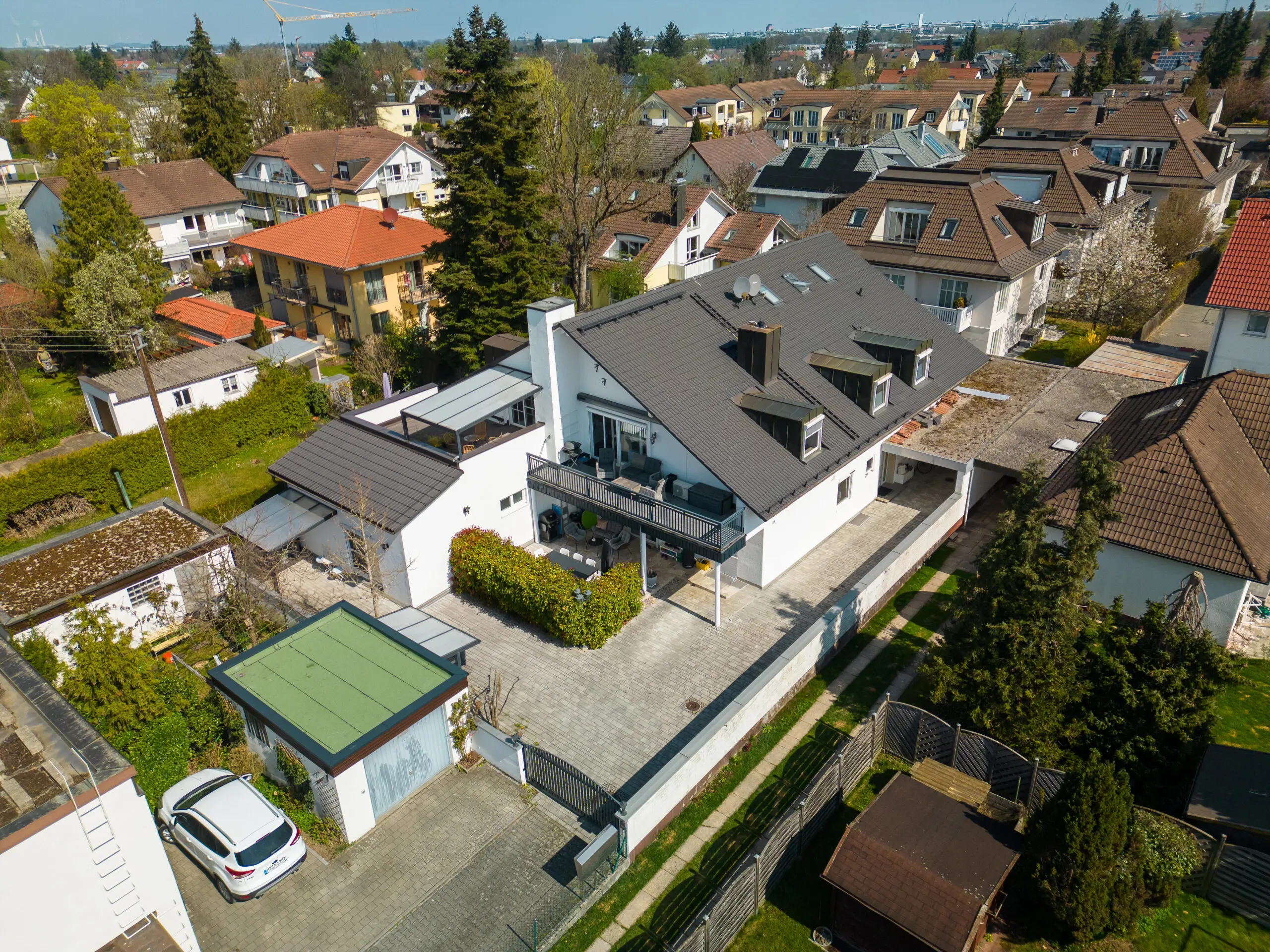 Luftaufnahme eines modernen zweistöckigen Hauses mit grauem Dach, Auffahrt, Garage und umliegender Wohngegend.
